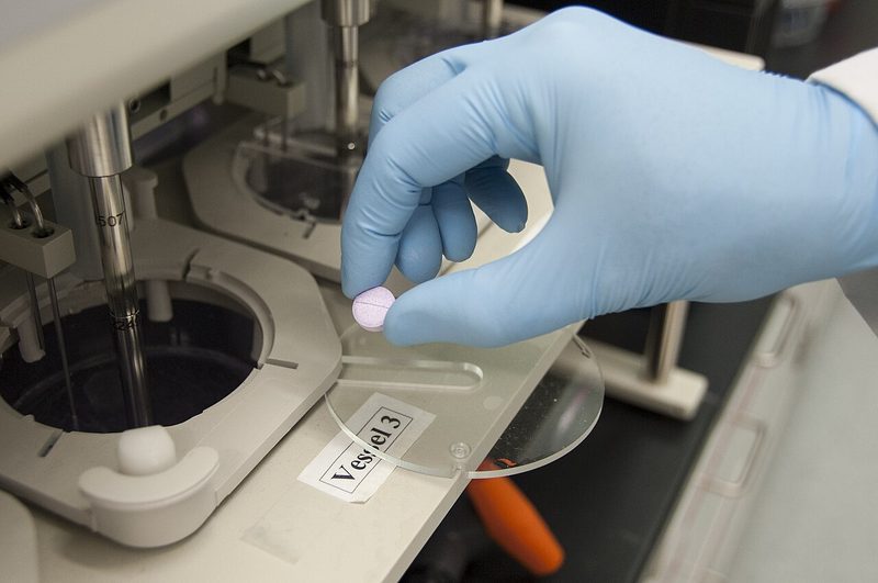 Gloved technician loading a tablet into a dissolution tester